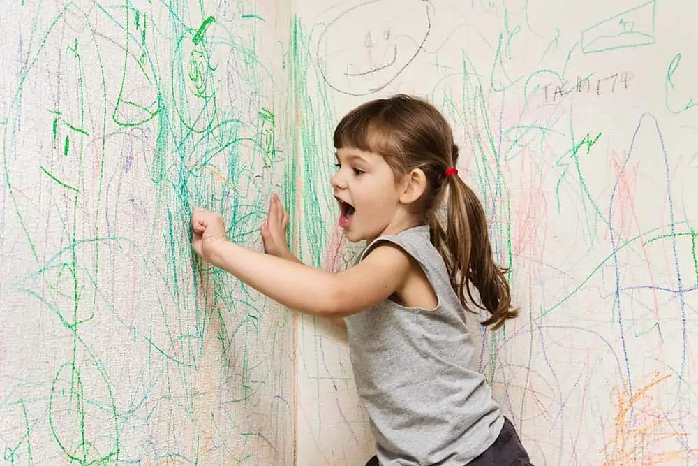 child coloring the wall with crayons