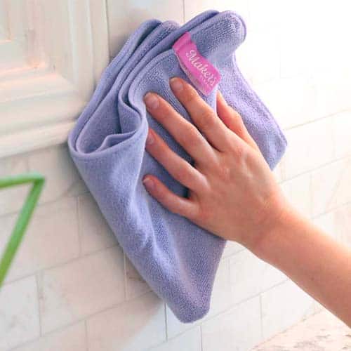 A hand using a purple microfiber cloth to clean tiles